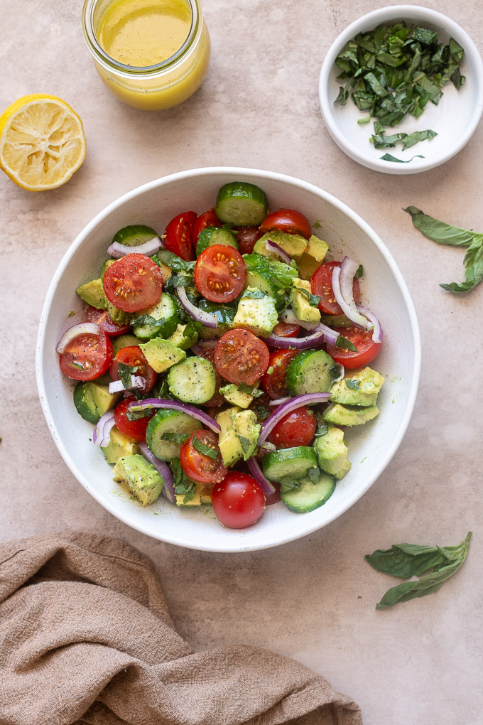 Cucumber tomato avocado salad in a bowl with fresh basil.