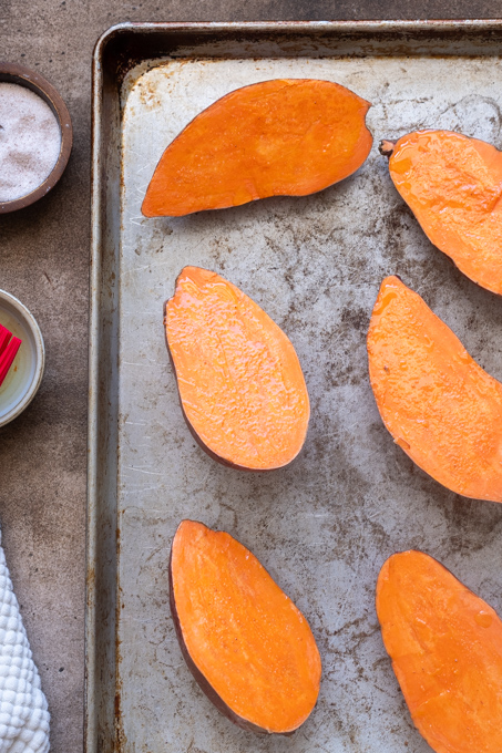 Halved sweet potatoes on a baking sheet with oil and salt.