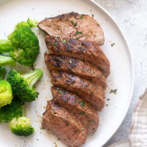 Juicy grilled pork tenderloin on a plate with broccoli.