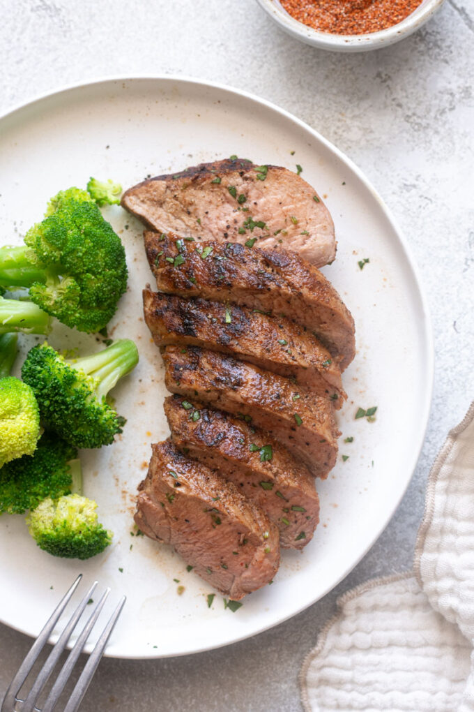 Juicy grilled pork tenderloin on a plate with broccoli.