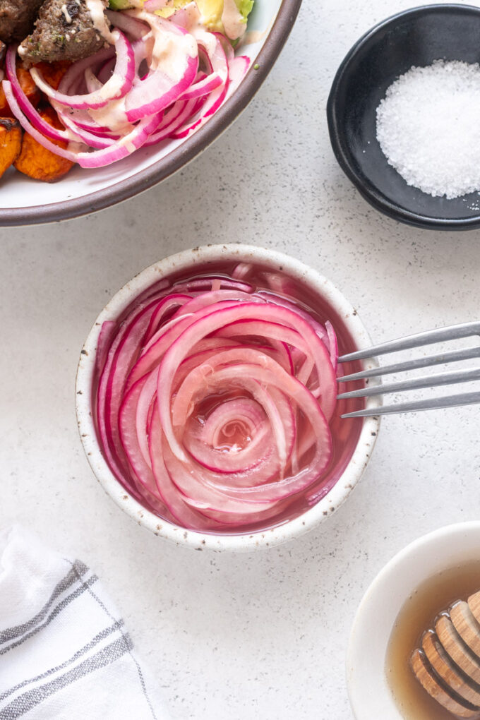 Quick pickled red onions in a small bowl with fork.