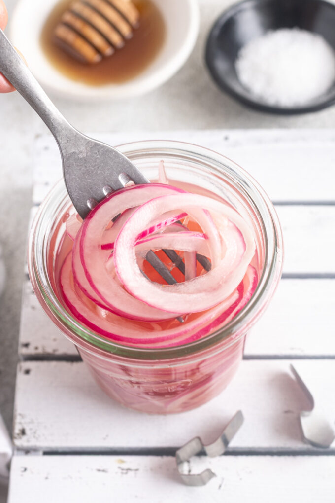 Fork pulling quick pickled red onions out of a jar.