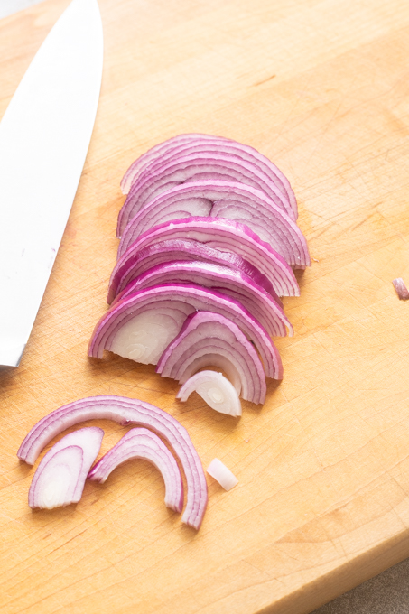 Red onion sliced with a knife on a cutting board.