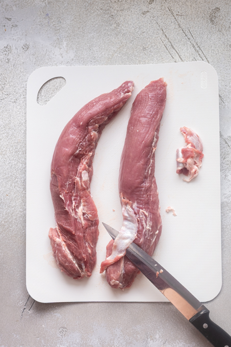 Knife cutting silver skin from pork tenderloin.