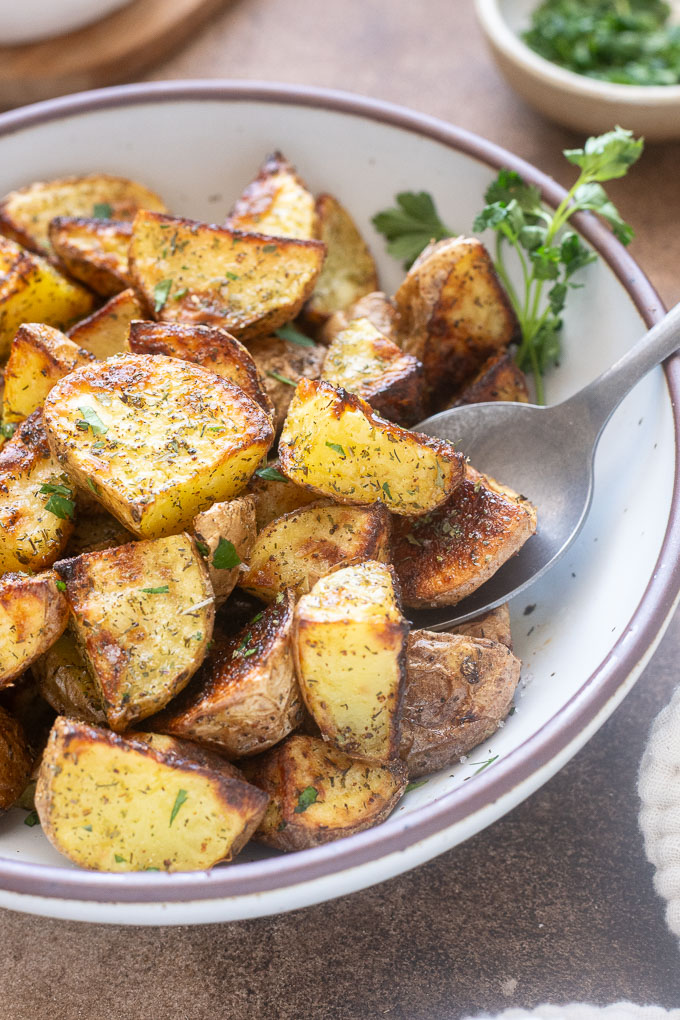 Roasted ranch potatoes in a bowl in with serving spoon.
