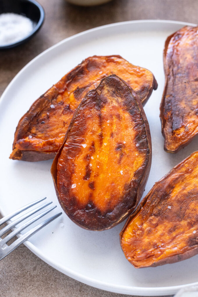 Roasted sweet potato halves with caramelized edges and sea salt on a plate.