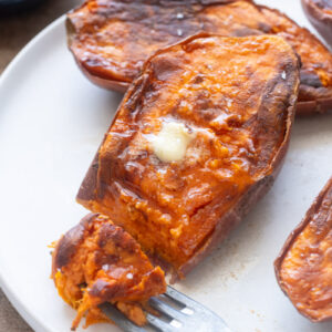 Caramelized roasted sweet potato halves with melted butter and flaky sea salt on a plate.