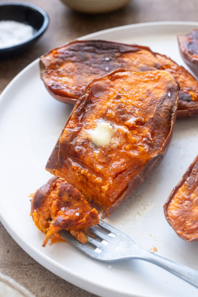 Caramelized roasted sweet potato halves with melted butter and flaky sea salt on a plate.