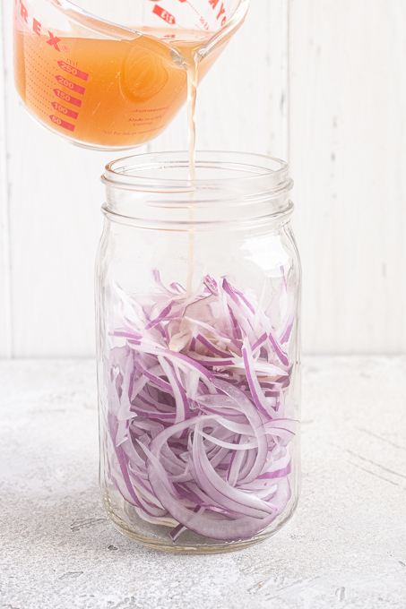 Sliced onions in jar with brine pouring over the top.