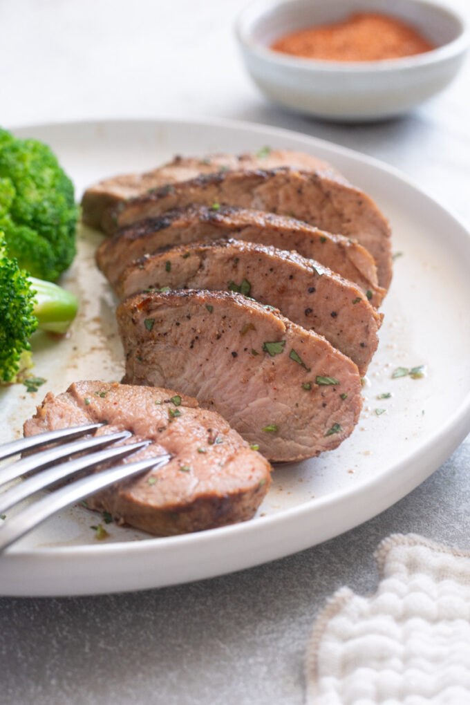 Juicy slices of grilled pork tenderloin on a plate with broccoli.