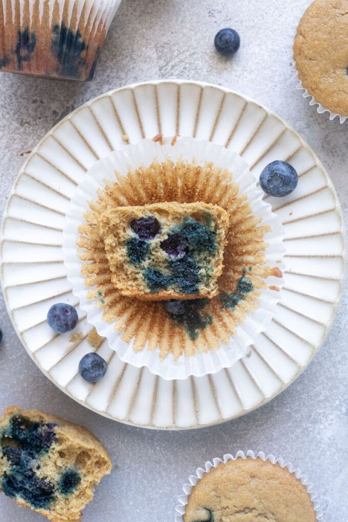 Fluffy blueberry oat flour muffin cut in half on a plate with blueberries.