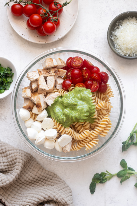 Chicken pesto pasta salad ingredients in mixing bowl before tossing.