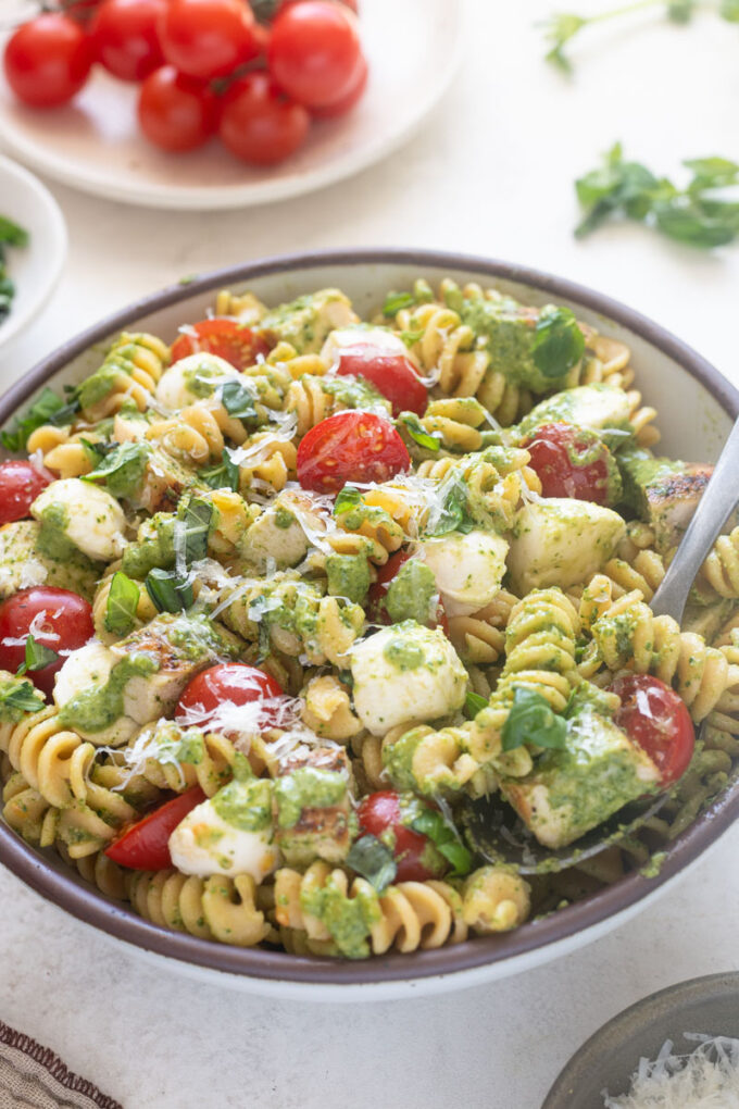Chicken pesto pasta salad in serving bowl with spoon digging in.