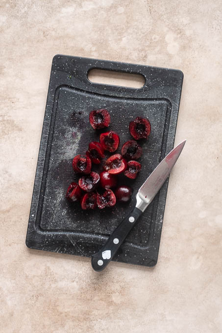 Halved cherries for fresh cherry crisp on cutting board.