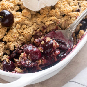 Spoonful of fresh cherry crisp in baking dish with ice cream.