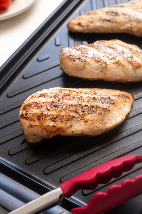 Grilled chicken for chicken pesto pasta salad on cutting board.