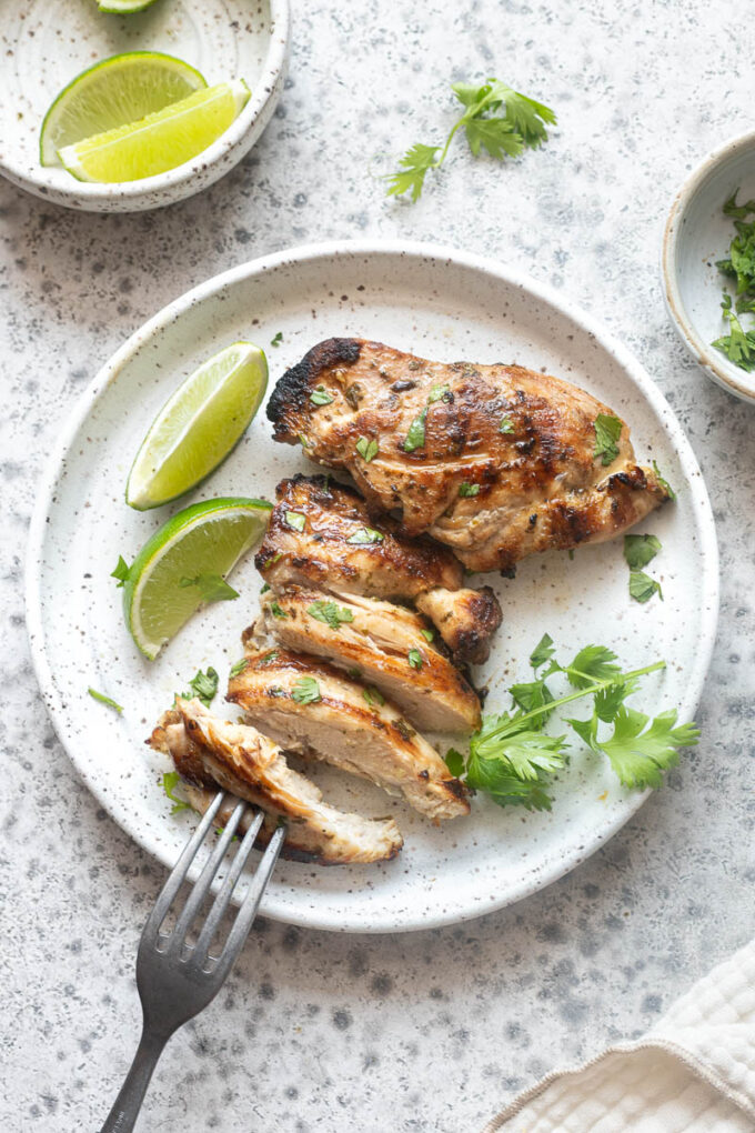 Grilled cilantro lime chicken sliced on a dinner plate with lime wedges.