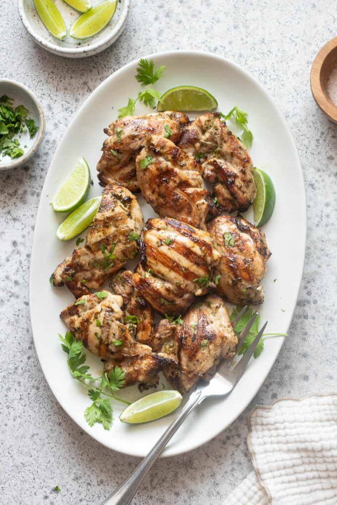 Grilled cilantro lime chicken on a platter with lime wedges and cilantro.