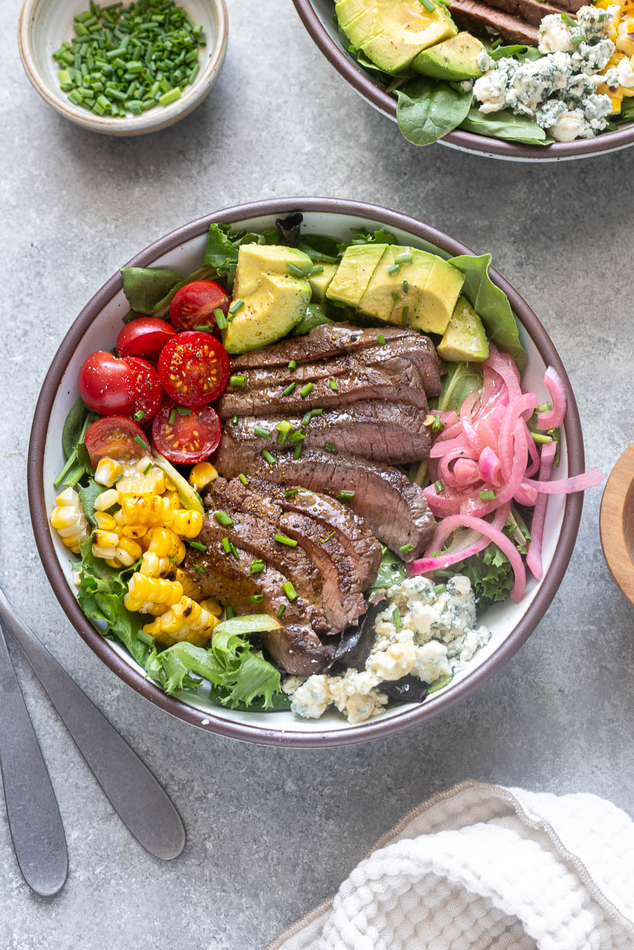 Grilled steak salad in bowl with chopped chives on top.