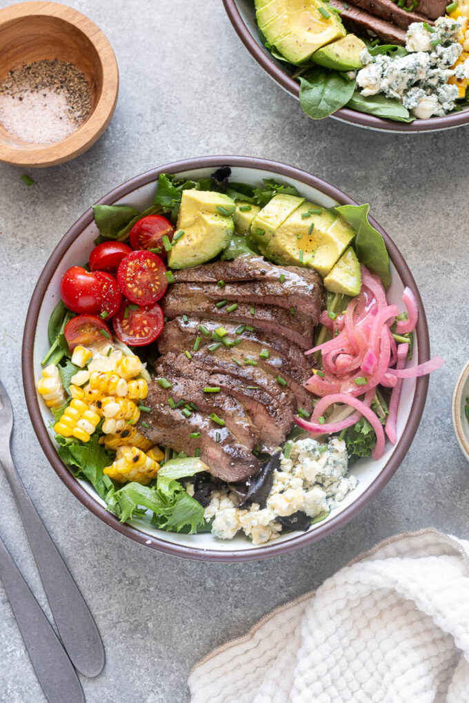 Summer steak salad with sliced steak, corn, avocado, tomatoes, blue cheese and pickled red onions.