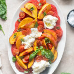 Tomato peach burrata salad on a platter with serving spoon.