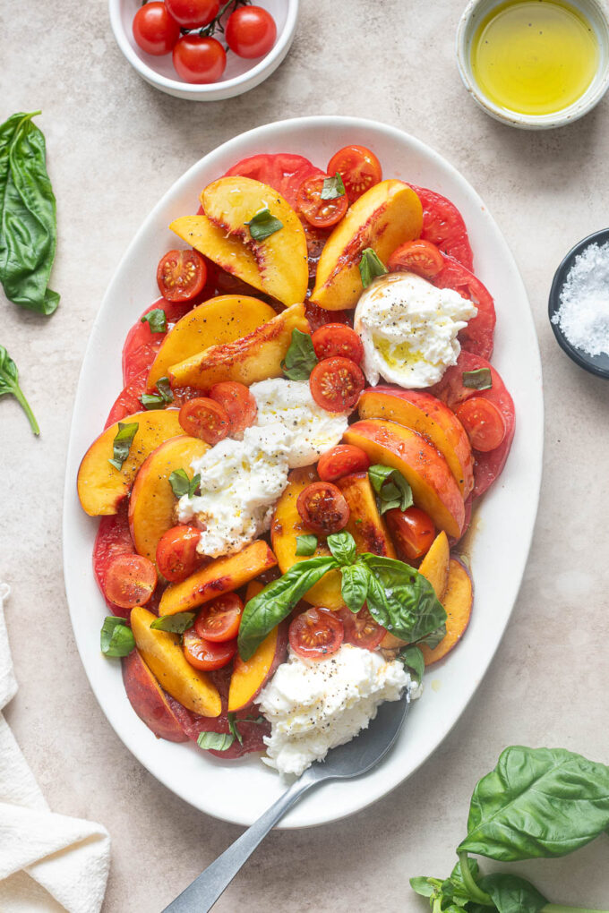Tomato peach burrata salad on a platter with serving spoon.