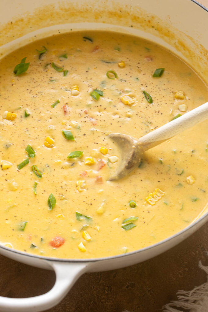 Creamy zucchini and corn chowder with potatoes, bacon and green onions in a white Dutch oven.