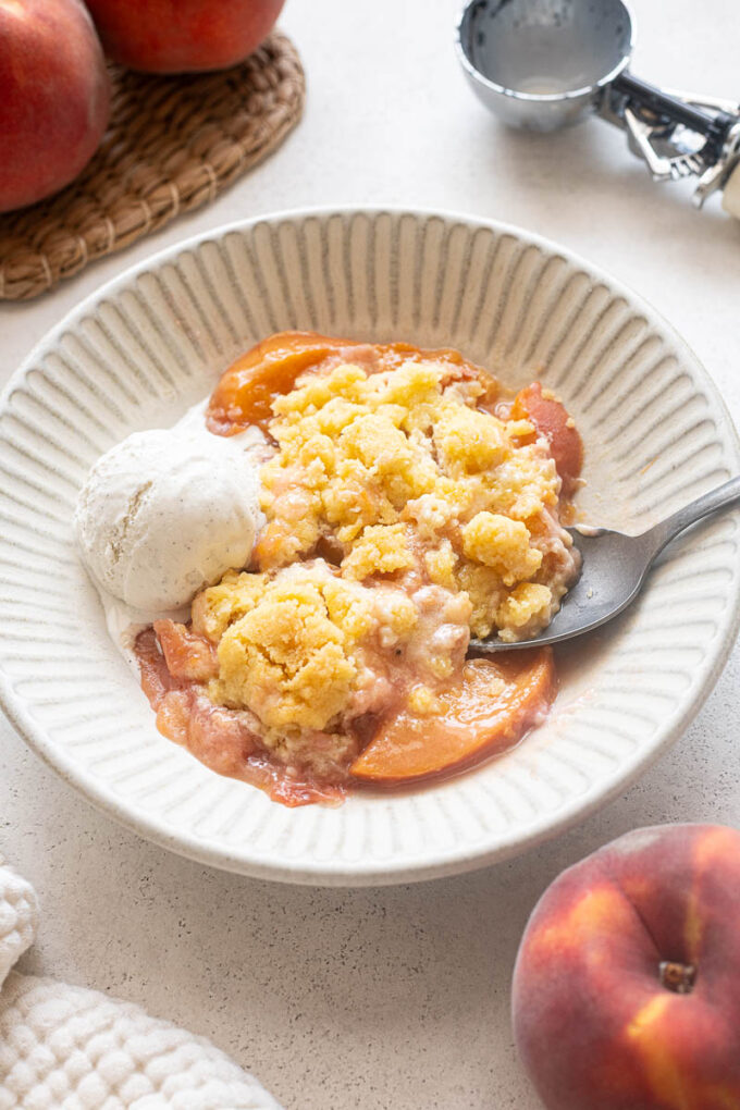 Serving of fresh peach cobbler in a bowl with ice cream.
