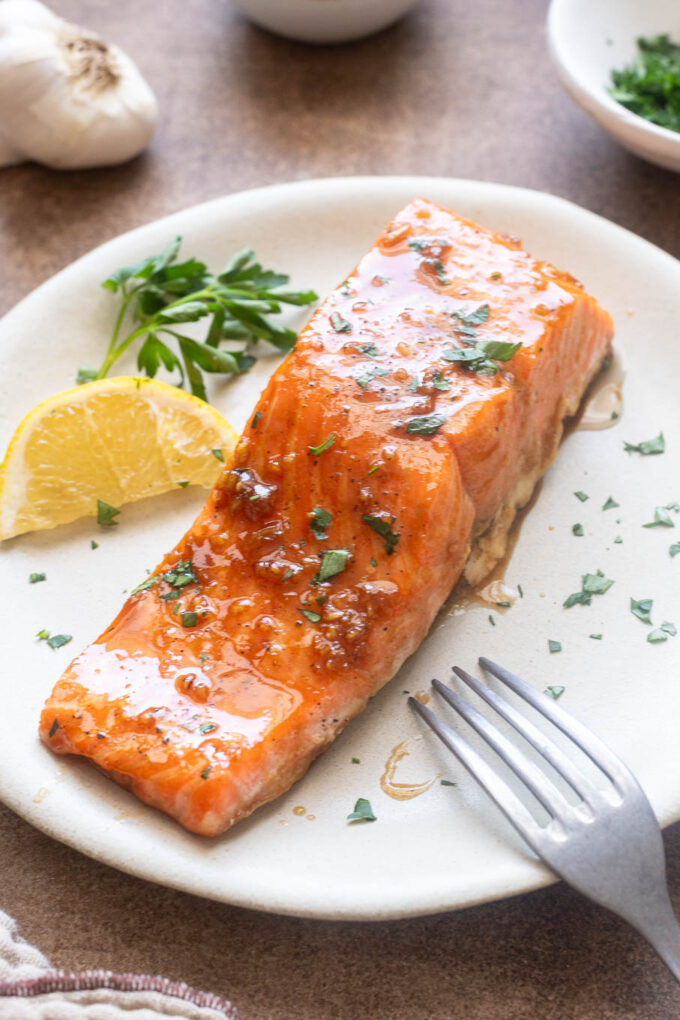 Honey garlic salmon filet on a plate with parsley and lemon.