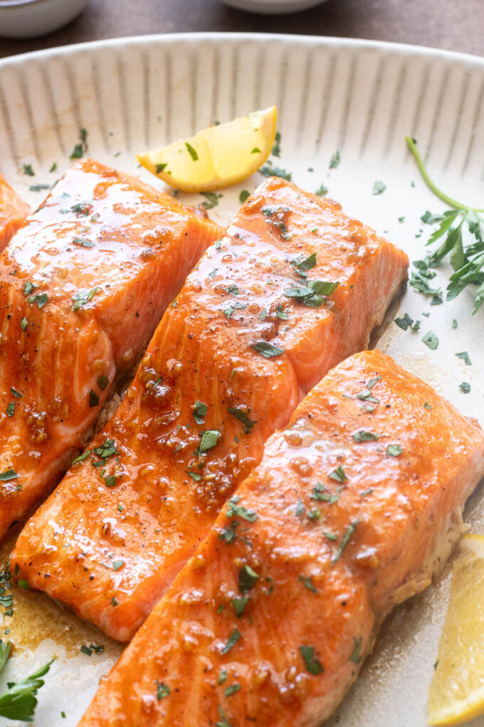 Honey garlic salmon on a platter with parsley and lemon.