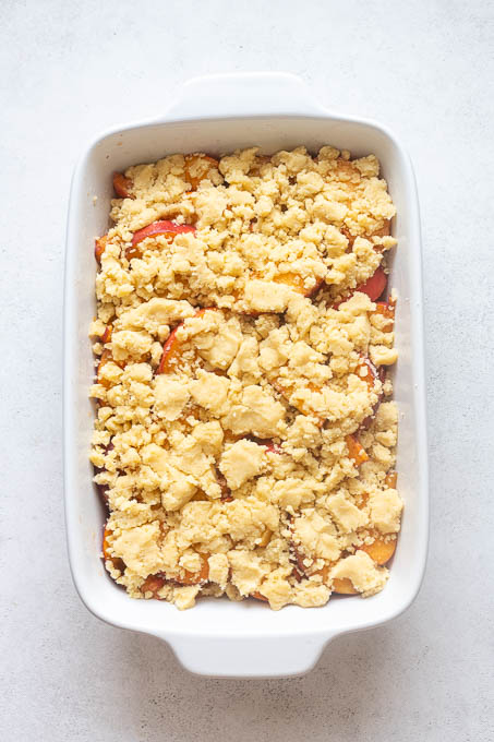 Fresh peach cobbler topped with large pieces of shortbread cookie dough before baking.