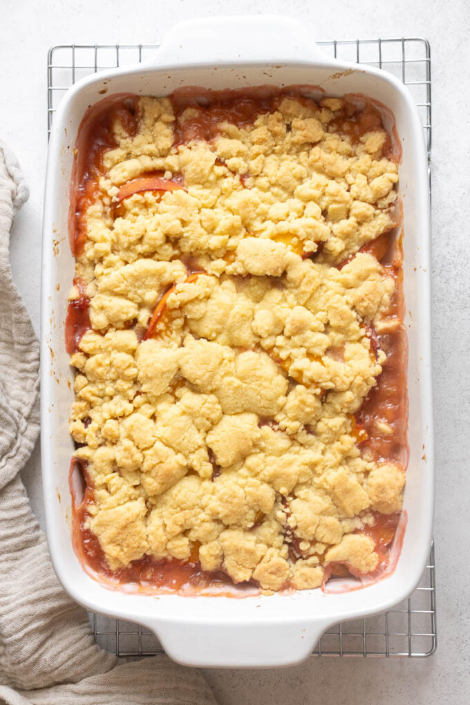 Peach cobbler with fresh peaches cooling on wire rack.