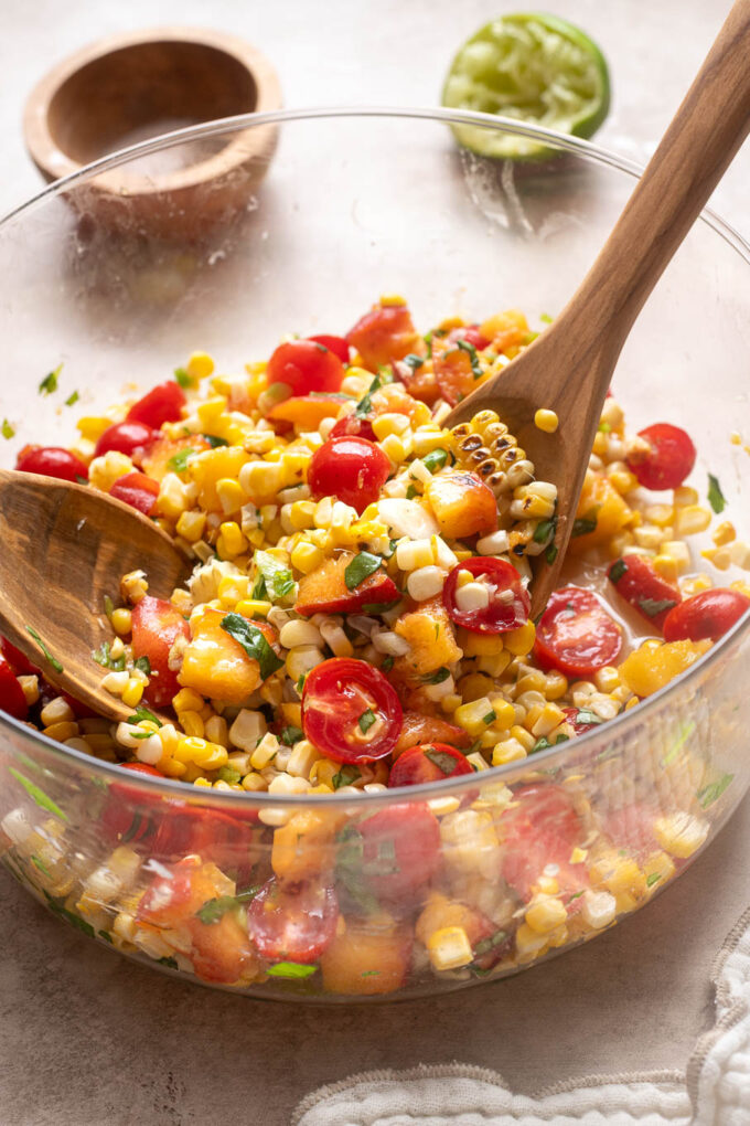 Fresh peach tomato corn salad tossed with grilled corn, basil, green onion and lime juice in a glass bowl.
