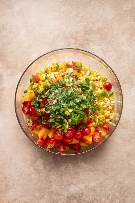 Ingredients for peach tomato corn salad in a bowl.