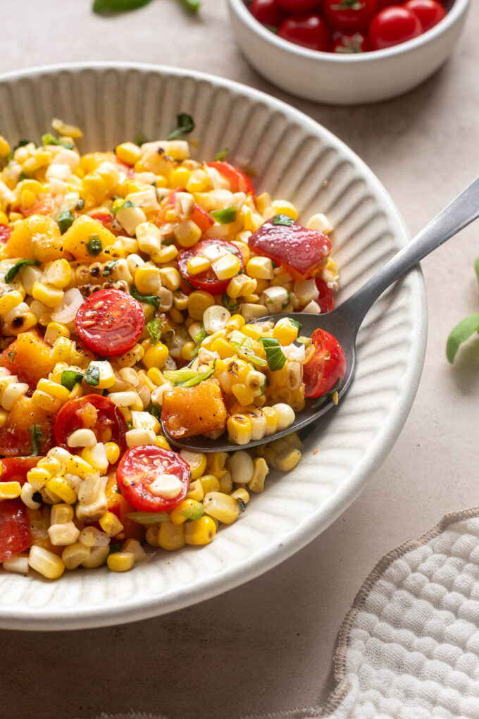 Spoonful of peach corn salad with cherry tomatoes, grilled corn and fresh basil.