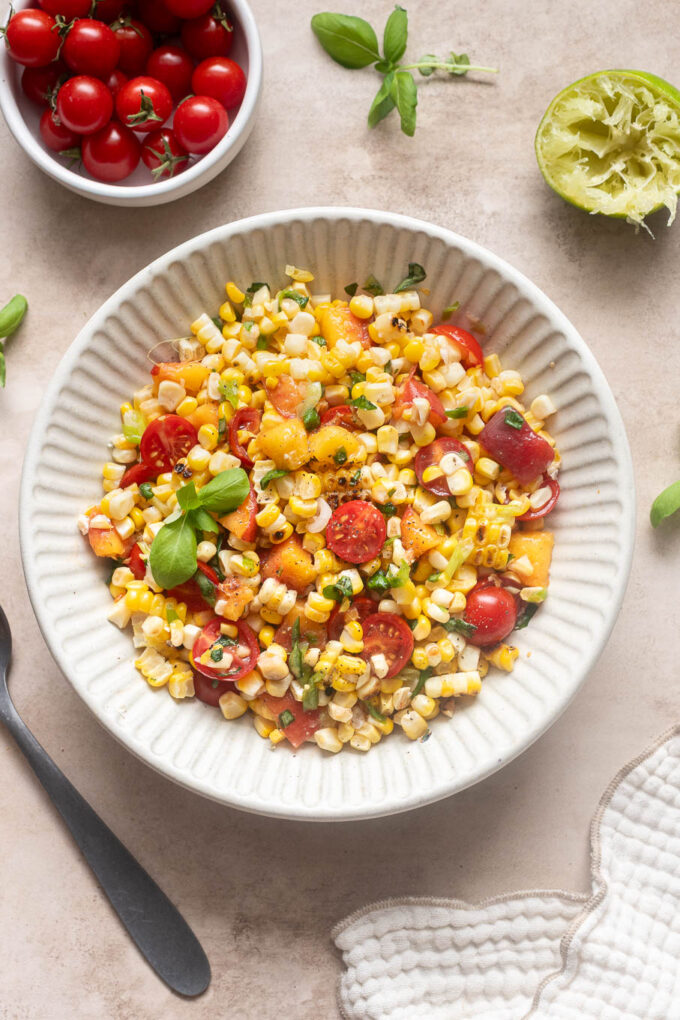 Overhead view of grilled corn salad with peaches, cherry tomatoes, green onions and fresh basil.