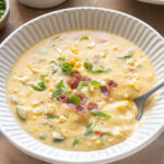 Zucchini corn chowder with bacon in a bowl with spoon digging in.