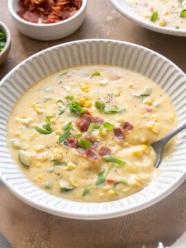 Zucchini corn chowder with bacon in a bowl with spoon digging in.