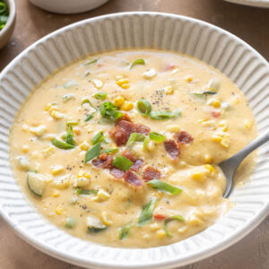 Zucchini corn chowder with bacon in a bowl with spoon digging in.