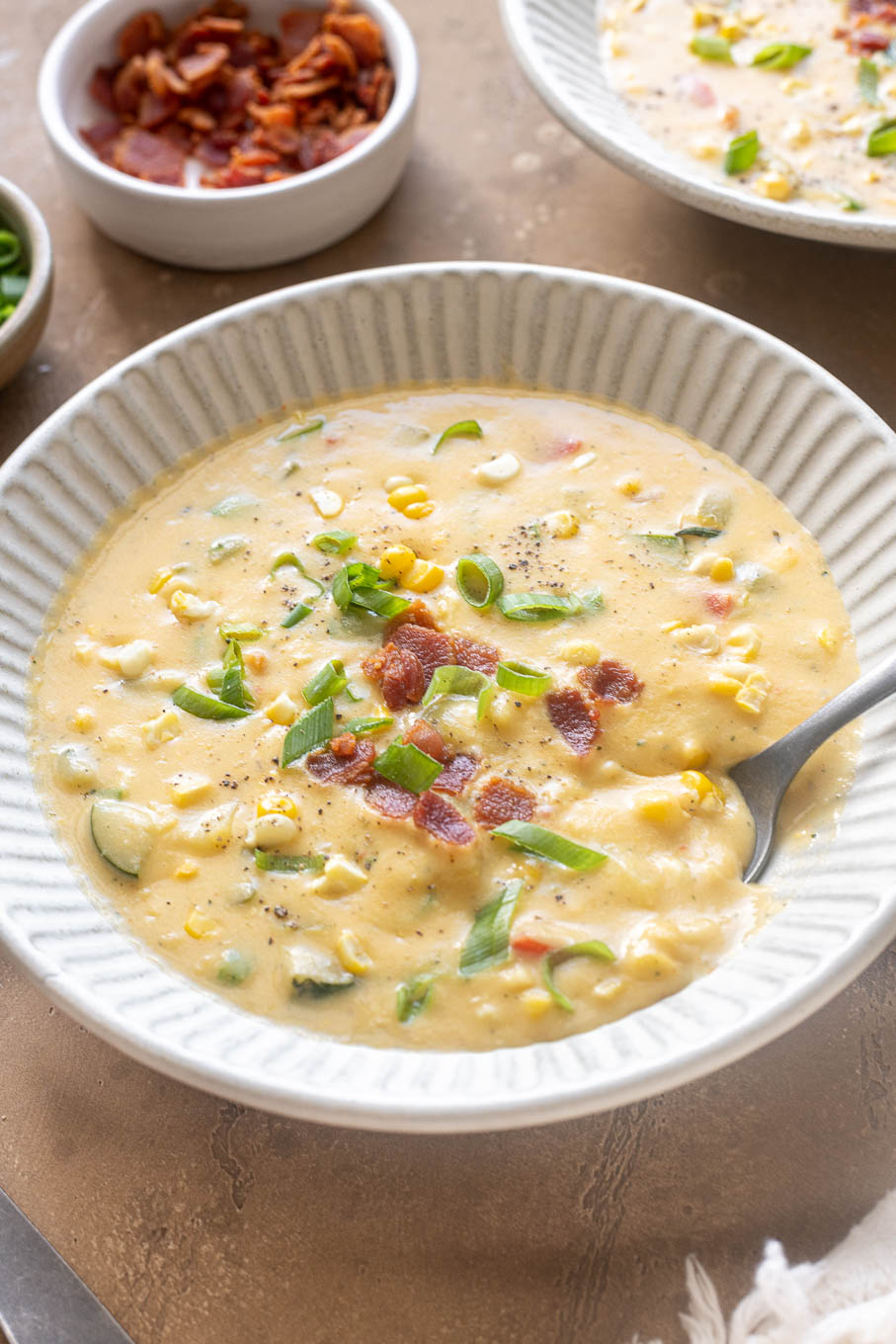 Zucchini corn chowder with bacon in a bowl with spoon digging in.