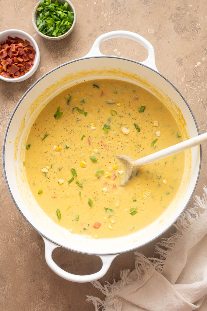 Overhead view of homemade zucchini corn chowder with bacon and vegetables in a white Dutch oven.