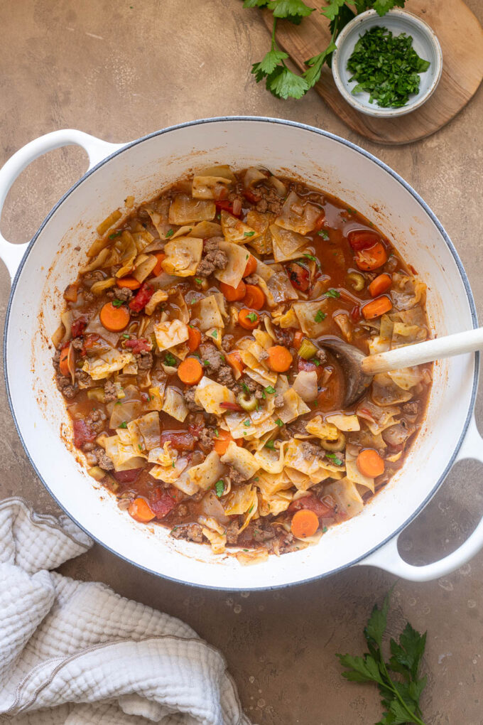 Ground beef and cabbage soup with carrots, celery and tomatoes in a white Dutch oven.