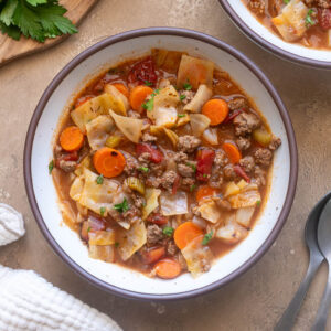 Ground beef cabbage soup with carrots, tomatoes and celery in a bowl garnished with fresh parsley.