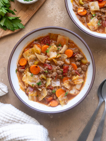 Ground beef cabbage soup with carrots, tomatoes and celery in a bowl garnished with fresh parsley.