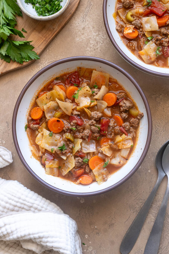 Ground beef cabbage soup with carrots, tomatoes and celery in a bowl garnished with fresh parsley.