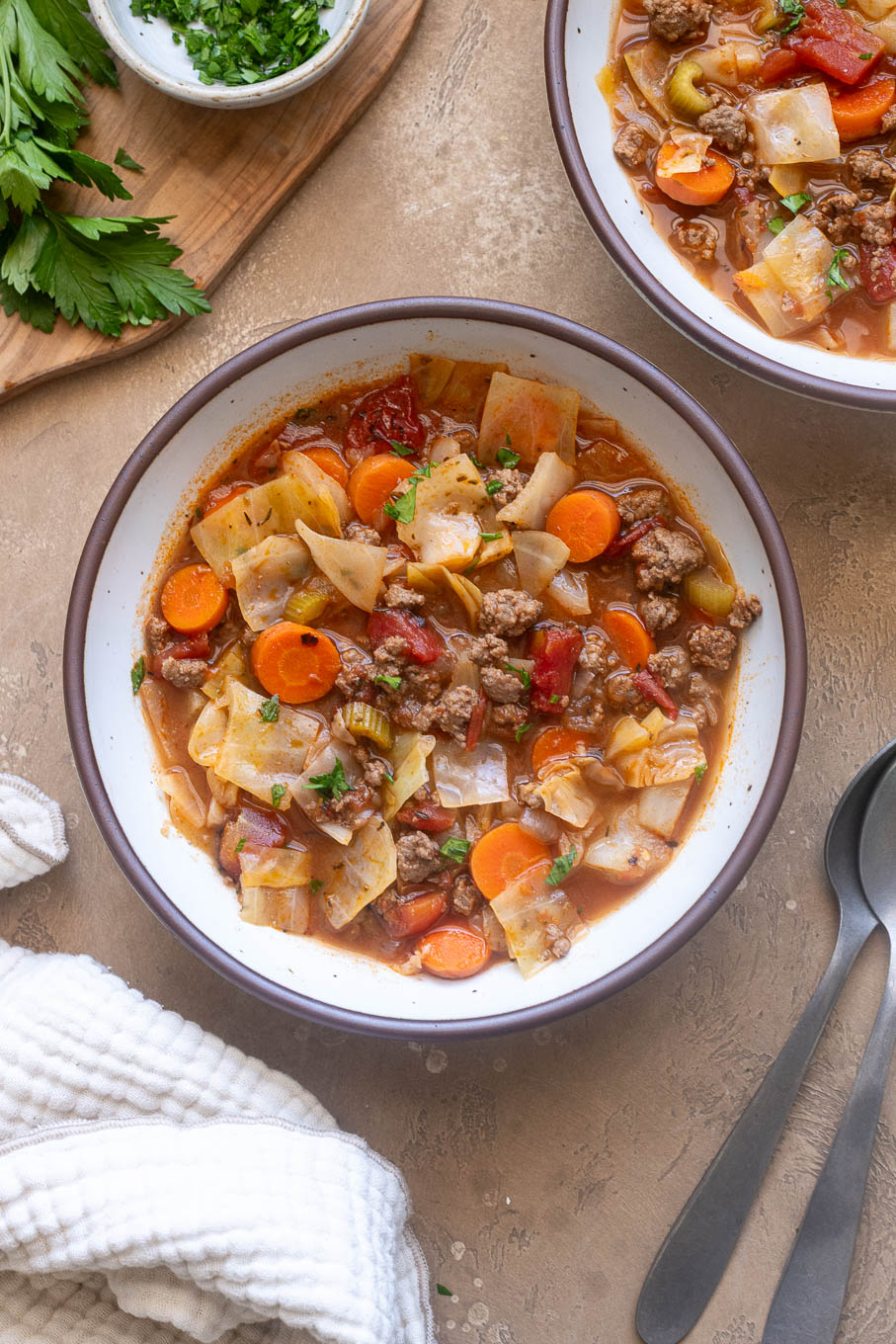 Ground beef cabbage soup with carrots, tomatoes and celery in a bowl garnished with fresh parsley.