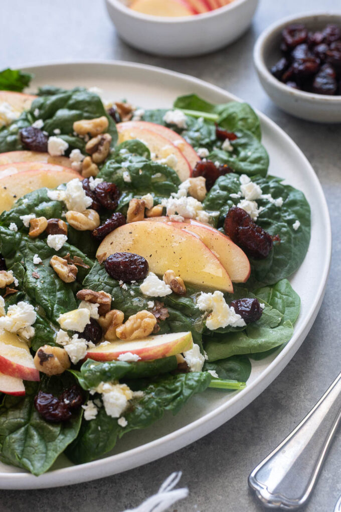 Close up of spinach and apple salad on a plate with feta and walnuts.