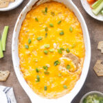 High protein buffalo chicken dip in a white baking dish with crackers and veggies.