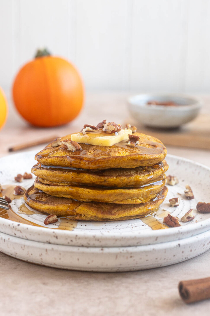 Stack of fluffy pumpkin oat flour pancakes topped with butter and maple syrup.