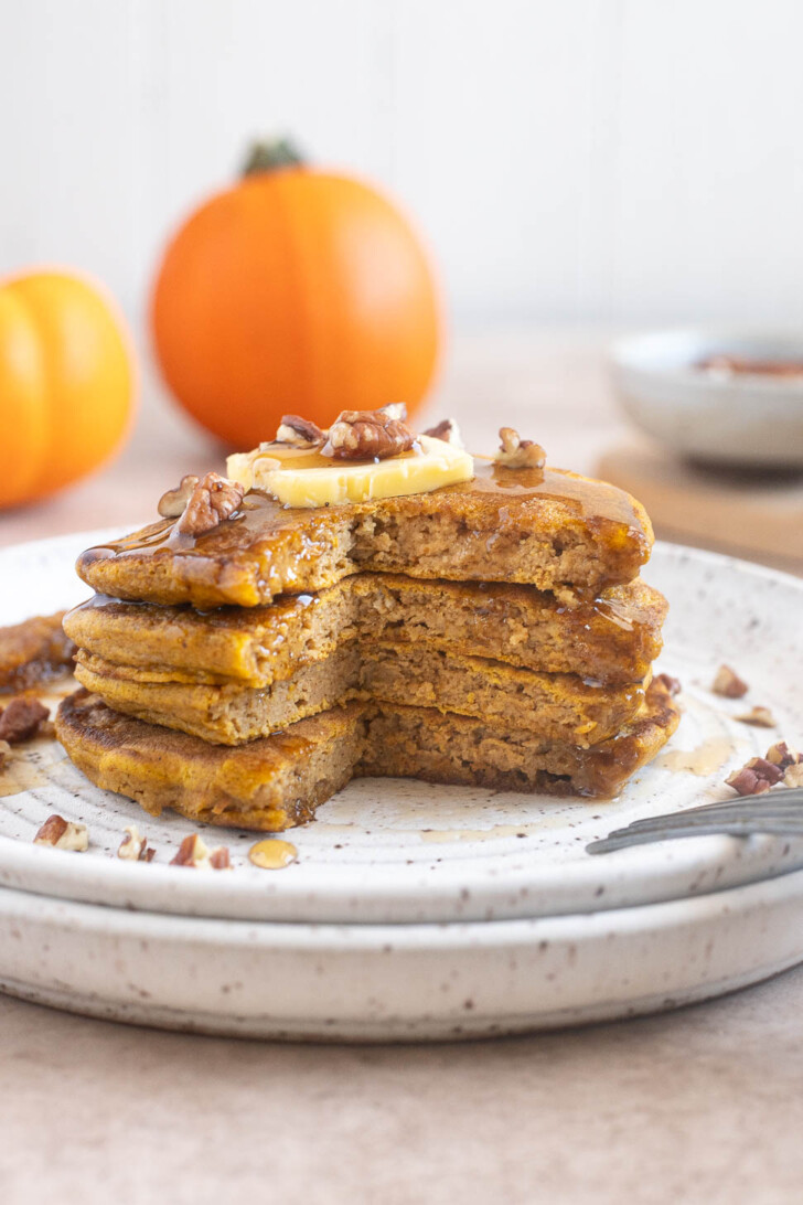 Stack of pumpkin oat flour pancakes cut open to reveal their soft, fluffy interior.